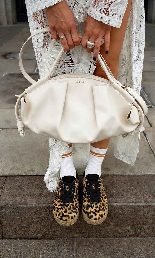 ALIX CHICA COMBINA VESTIDO BLANCO DE ENCAJE CON ABERTURA EN PIERNA Y SNEAKERS LEOPARDO CON CALCETAS Y BOLSO LOEWE DE MANO