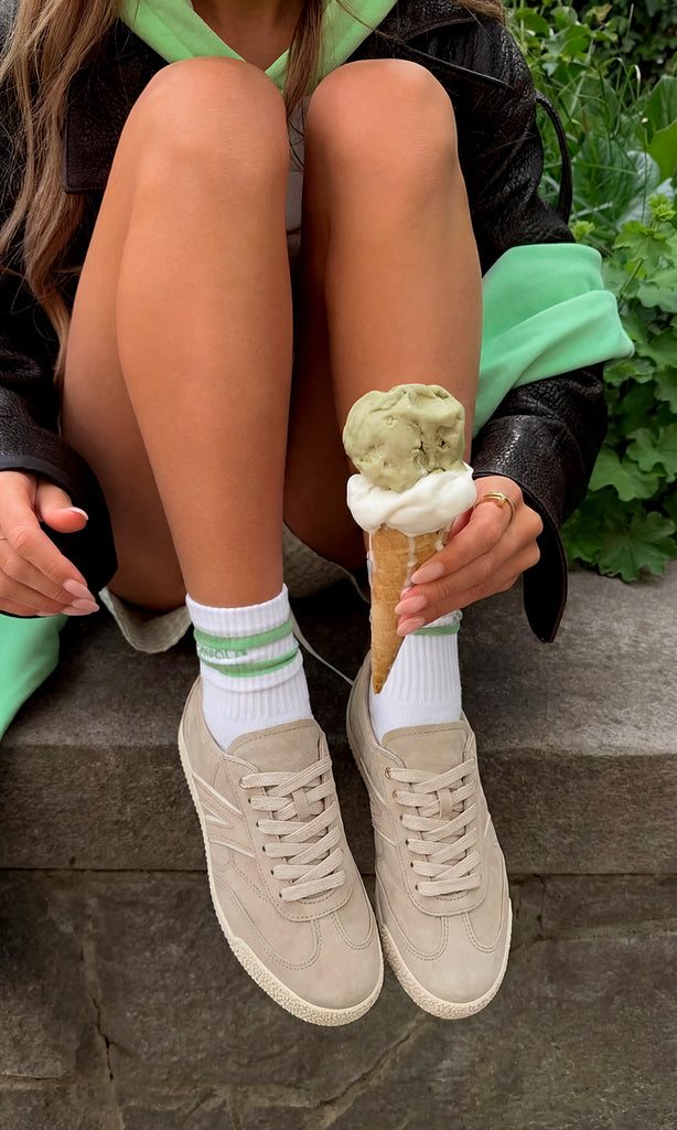 ALIX TENIS COLOR NUDE CON CALCETAS BLANCAS Y SHORT CORTO CON GABARDINA CAFE DE CUERO ENCIMA DE SUDADERA VERDE MIENTRAS CHICA SOSTIENE HELADO