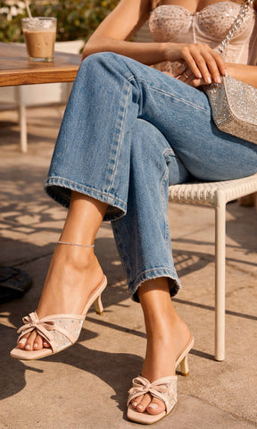 CAMELIA IT GIRL LUCE ZAPATILLAS NUDE CON MOÑO A JUEDO DE PANTALÓN DENIM Y BUSTIER MIENTRAS SOSTIENE BOLSO DE MANO