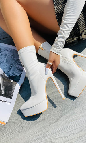 COUGAR MODELO POSA BOTINES BLANCOS CON BLUSA DE MANGA LARGA SOBRE PISO DE MADERA PARA LLEVAR AUN BRUNCH CON AMIGAS