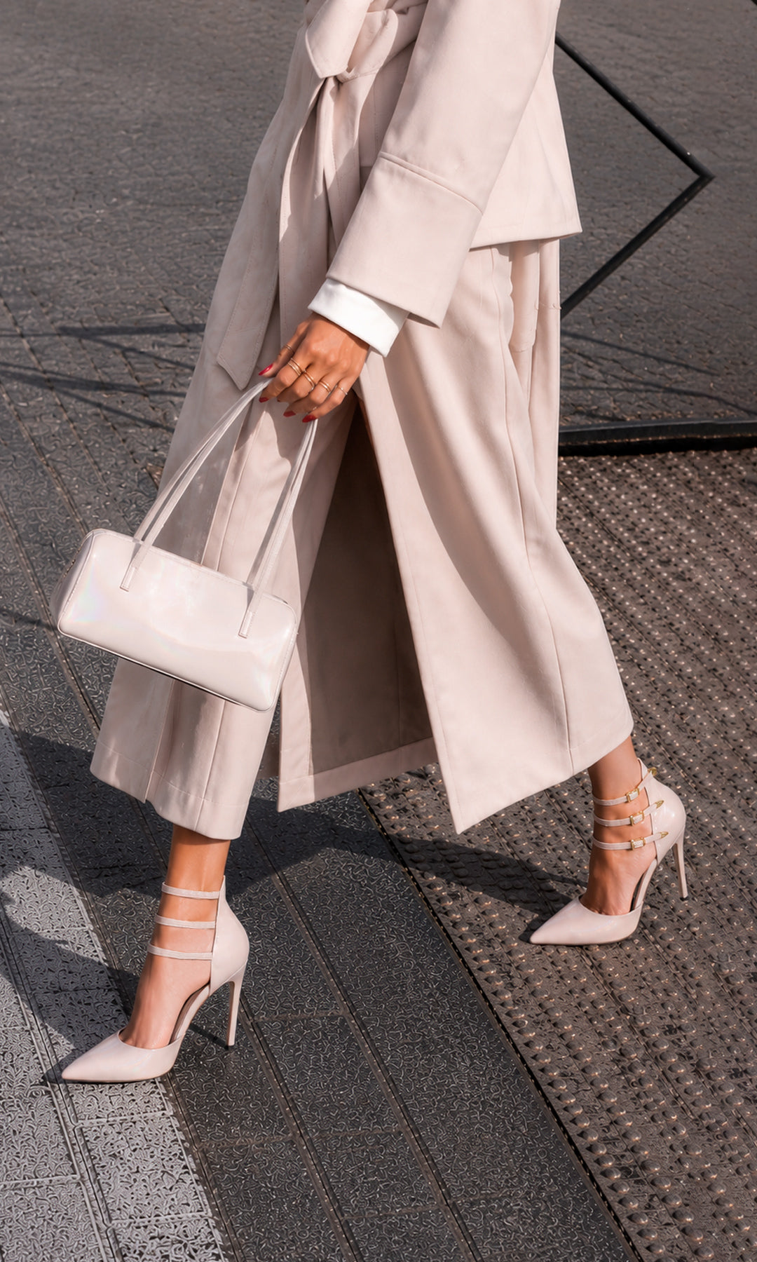 DEMON CHICA COMBINA ZAPATILLAS NUDE DE TACON ALTO MIENTRAS LUCE GABARDINA OVERSIZED CON CINTURON COLOR ARENA Y BOLSO DE MANO