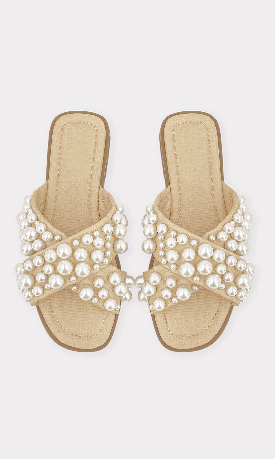 GRETA MODELO AGARRA SANDALIAS DE PISO CON PERLAS EN LA MANO CON LOOK DE PANTALON BEIGE Y BLUSA BLANCA PARA LLEVAR A LA PLAYA