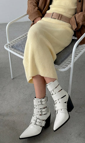 HOLSTER CHICA COMBINA BOTINES BLANCOS DE TACON CUADRADO CON VESTIDO AMARILLO LARGO MIENTRAS USA CHAMARRA CAFE Y CINTURON 
