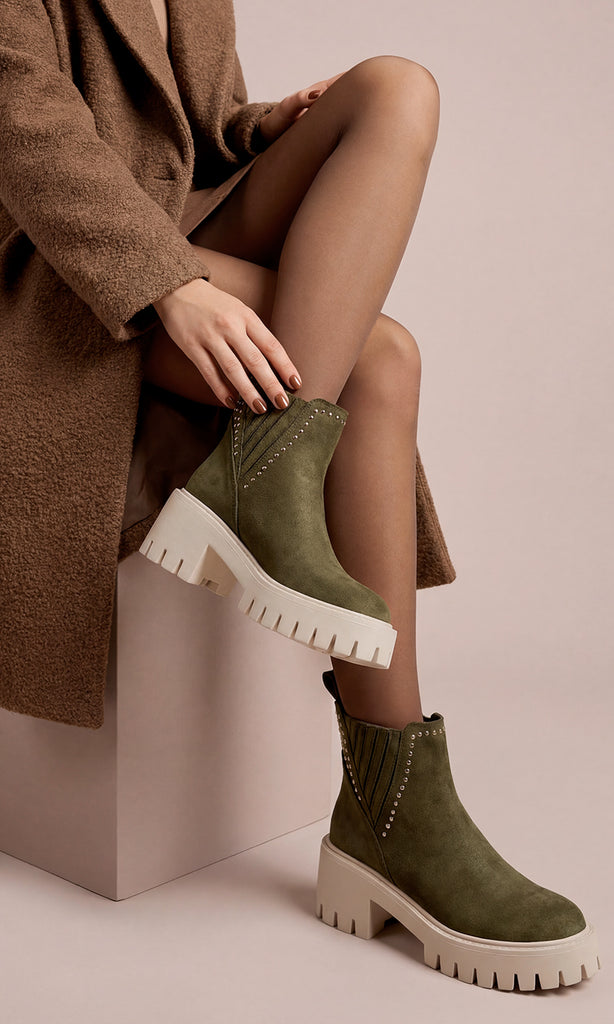 HONEY MODELO POSA SENTADA BOTINES COLOR VERDE OLIVO DE SUELA TRACK MIENTRAS USA MEDIAS TRANSPARENTES Y GABARDINA CAFE OVERSIZE