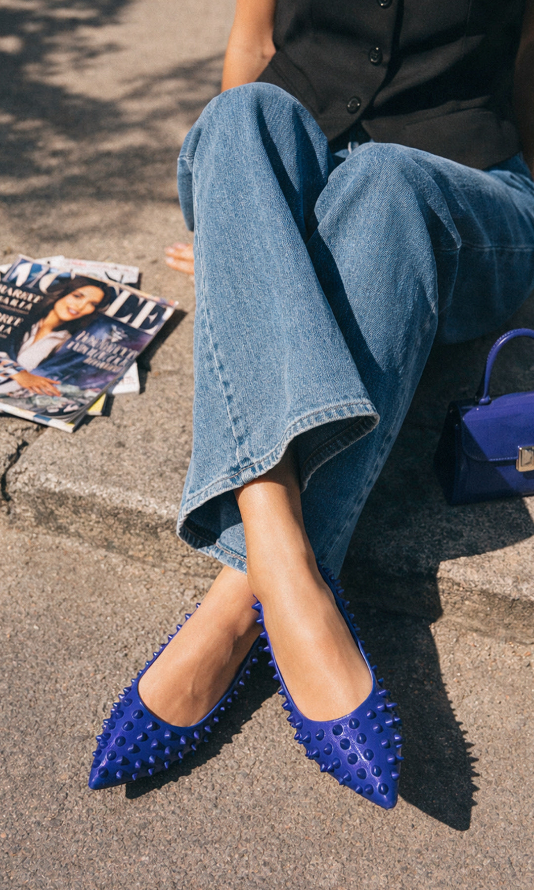KENDRA MODELO SENTADA SOBRE EL PISO POSA FLATS AZULES CON ESTOPEROLES USANDO PANTALON DE MEZCLILLA Y CHALECO SASTRE NEGRO PARA LA OFICINA