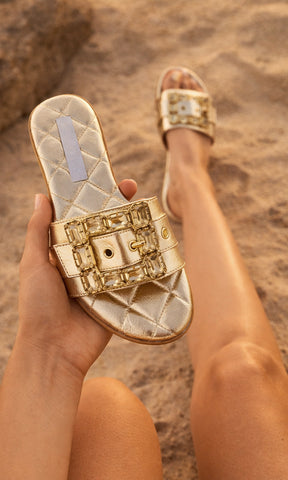 PRISCILA MODELO POSA EN LA PLAYA SANDALIAS DORADAS DE PISO MIENTRAS ESTÁ SENTADA EN LA ARENA Y LUCE TRAJE DE BAÑO DE DOS PIEZAS