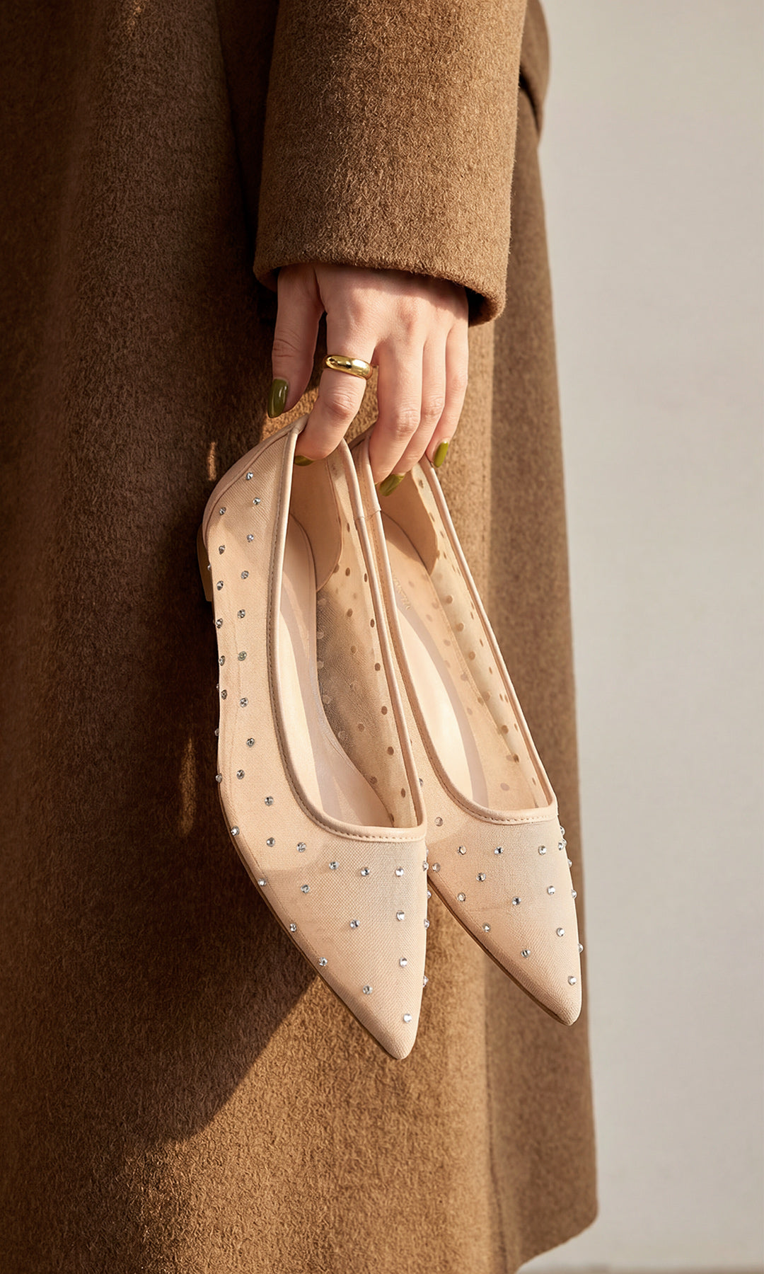 RENATTA CHICA COMBINA GABARDINA CAFE MIENTRAS SOSTIENE EN SU MANO FLATS COLOR NUDE CON BRILLOS Y JOYERIA MINIMALISTA PARA VERSE CHIC