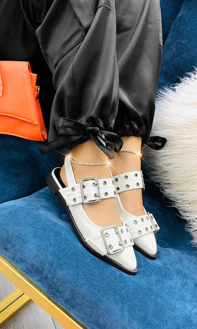 ROSALY CHICA SENTADA EN SILLA AZUL USA ZAPATOS BLANCOS DESTALONADOS CON PANTALON JOGGER DE VINIPIEL Y TOP BLANCO A JUEGO CON BOLSO NARANJA