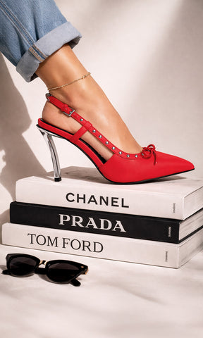 ZENITH MODELO POSA ZAPATILLAS SLINGBACK ROJAS DE TACÓN CROMADO MIENTRAS PISA LIBROS DE MODA EN SESIÓN FOTOGRÁFICA