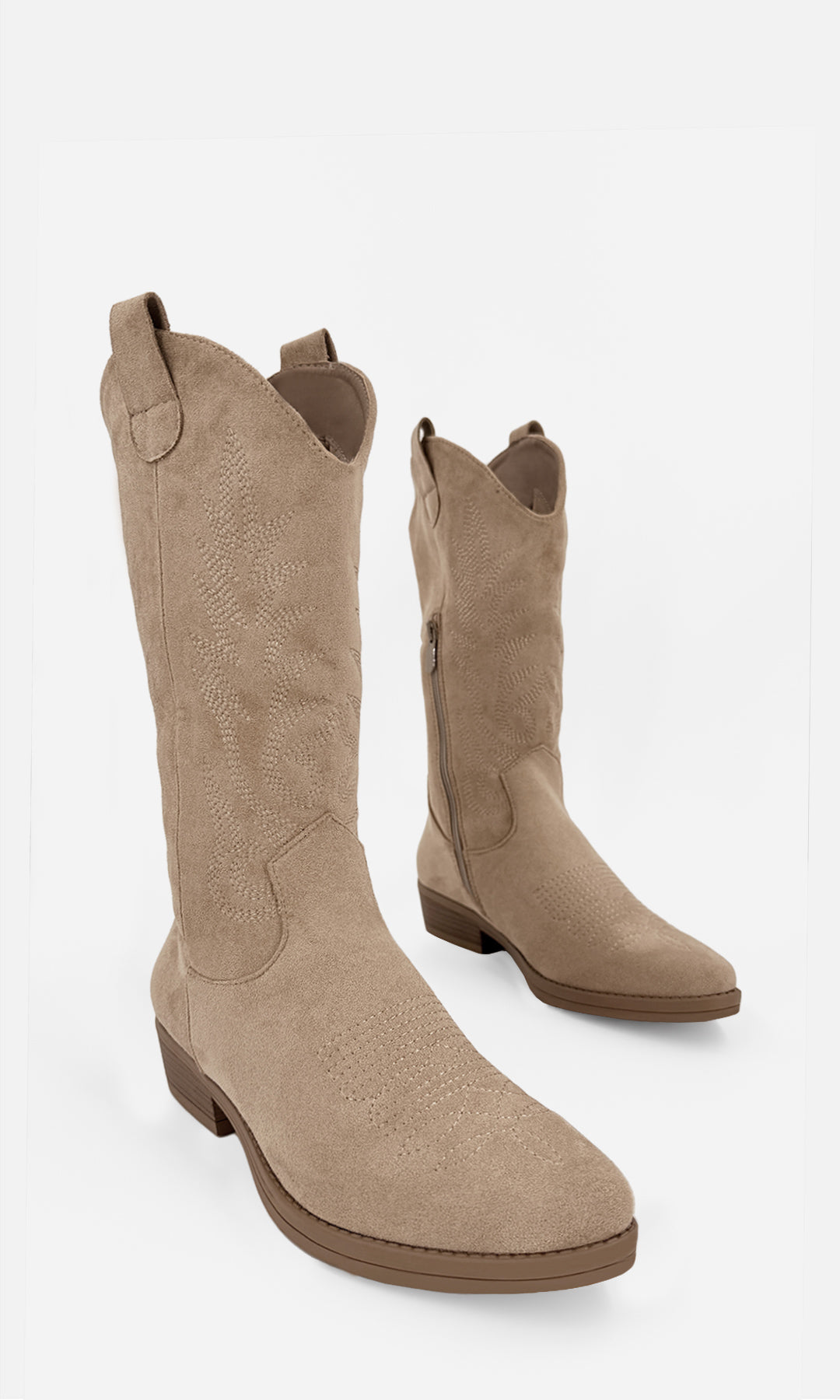 Vista en tres cuartos de botas vaqueras Arabella color nude de gamuza con bordado western, cierre lateral y tacón de 4 cm.