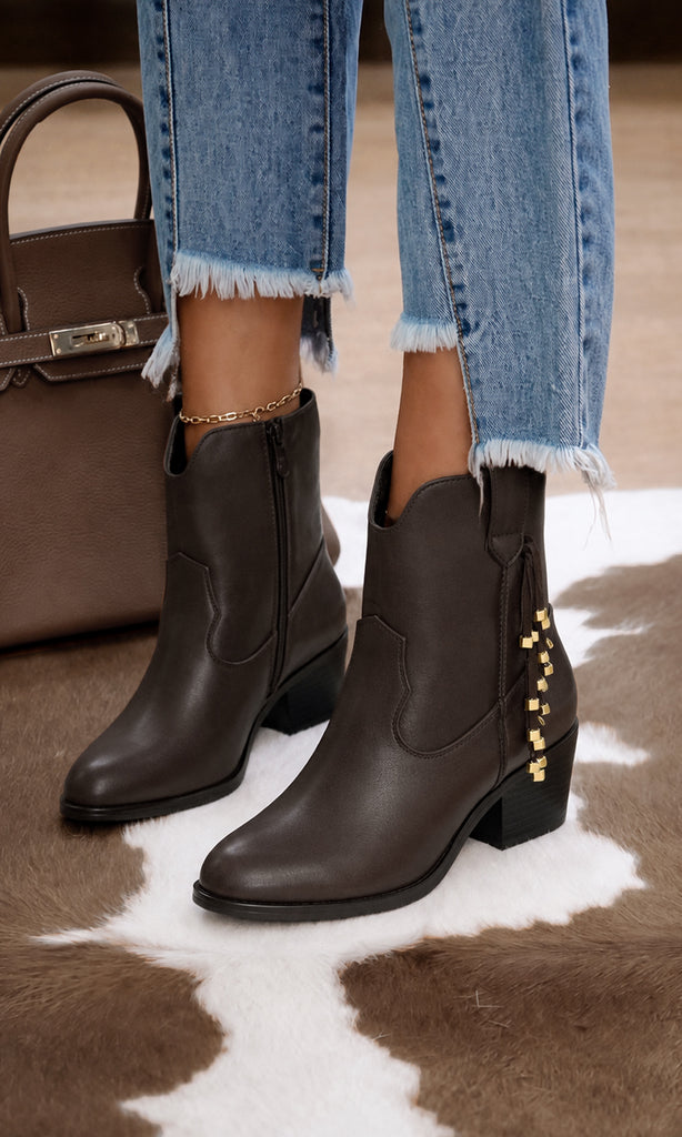 Botas Agatha color café estilo western con detalle de cadena dorada lateral y tacón bajo, combinadas con jeans para un look casual y sofisticado.
