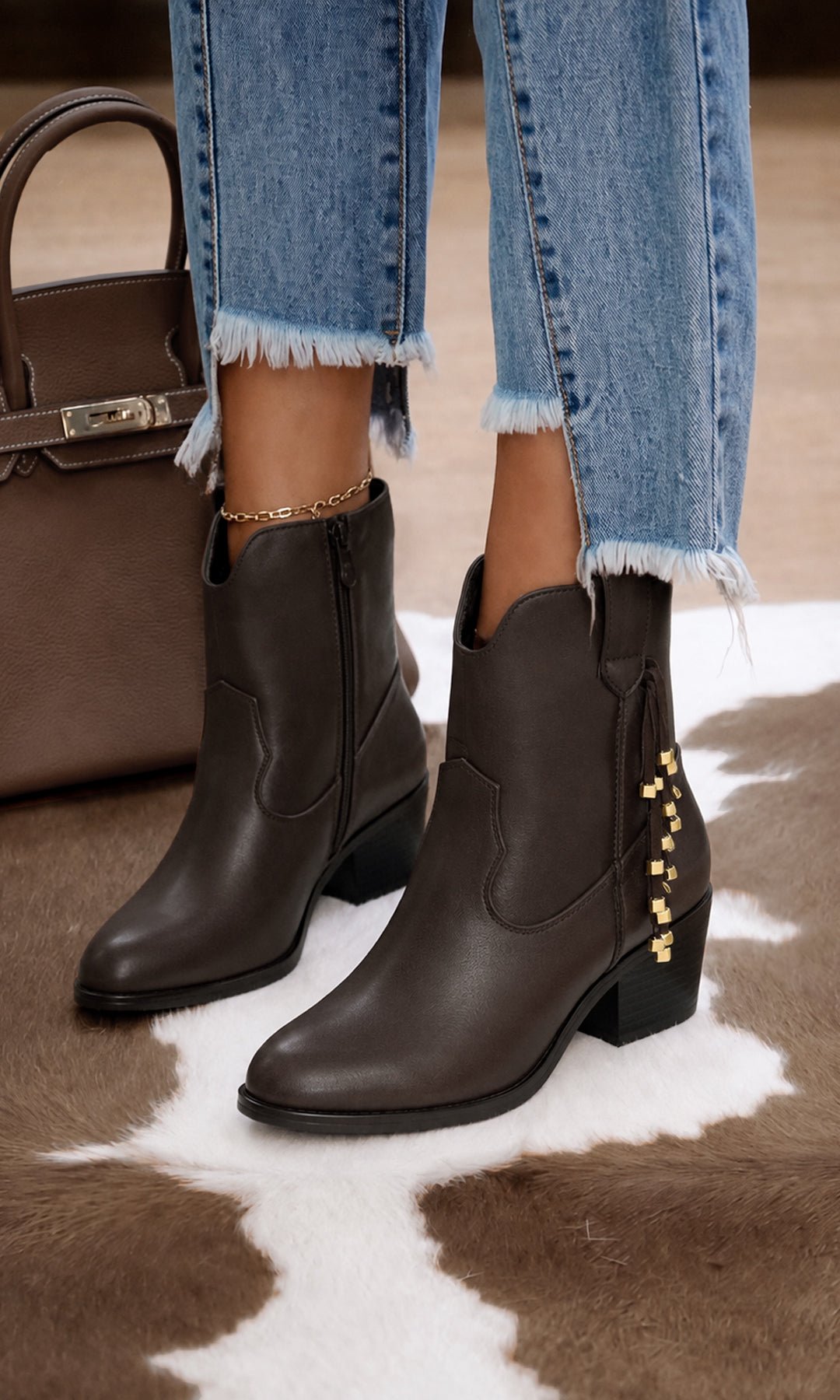 Botas Agatha color café estilo western con detalle de cadena dorada lateral y tacón bajo, combinadas con jeans para un look casual y sofisticado.