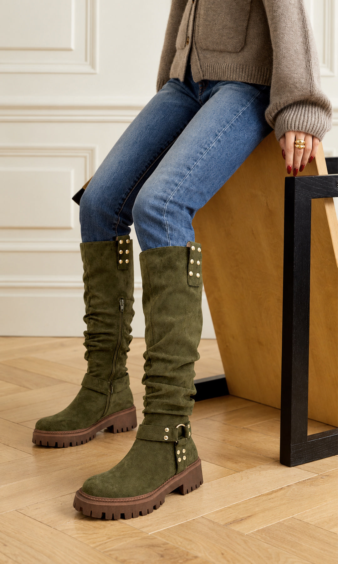 Botas altas verde olivo con acabado tipo gamuza, caña arrugada, suela track café y detalles dorados, combinadas con jeans azules y cardigan tejido para un look casual de otoño
