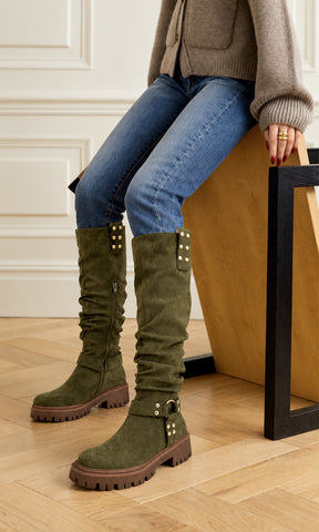 Botas altas verde olivo con acabado tipo gamuza, caña arrugada, suela track café y detalles dorados, combinadas con jeans azules y cardigan tejido para un look casual de otoño