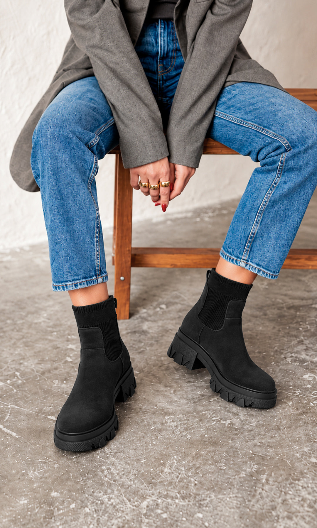 Botines Ashton negros estilo Chelsea con caña elástica de punto, suela track robusta y tacón chunky bajo, combinados con jeans azules y blazer gris en un look casual urbano