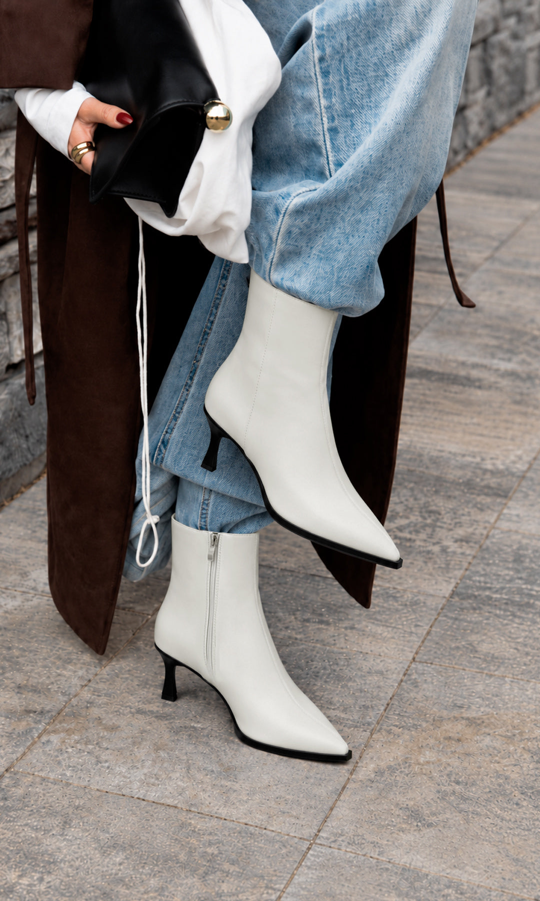 Botines blancos de tacón fino bajo y punta afilada, combinados con jeans claros de pierna ancha, blusa blanca y abrigo café en un look casual elegante para mujer