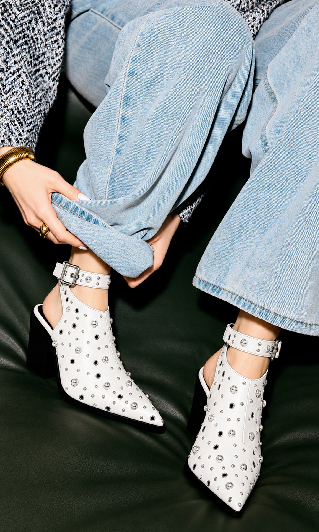 Botines destalonados blancos de tacón ancho y punta fina, decorados con estoperoles y ojillos metálicos, combinados con jeans claros de pierna ancha y suéter tejido en un look casual moderno