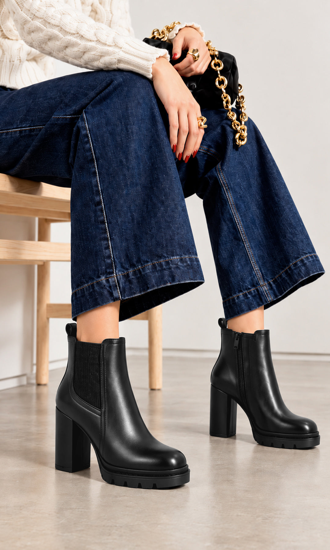 Botines negros para mujer estilo Chelsea con panel elástico lateral, cierre interno, tacón alto de bloque y suela track, combinados con jeans de pierna ancha y suéter de punto blanco en un look casual contemporáneo