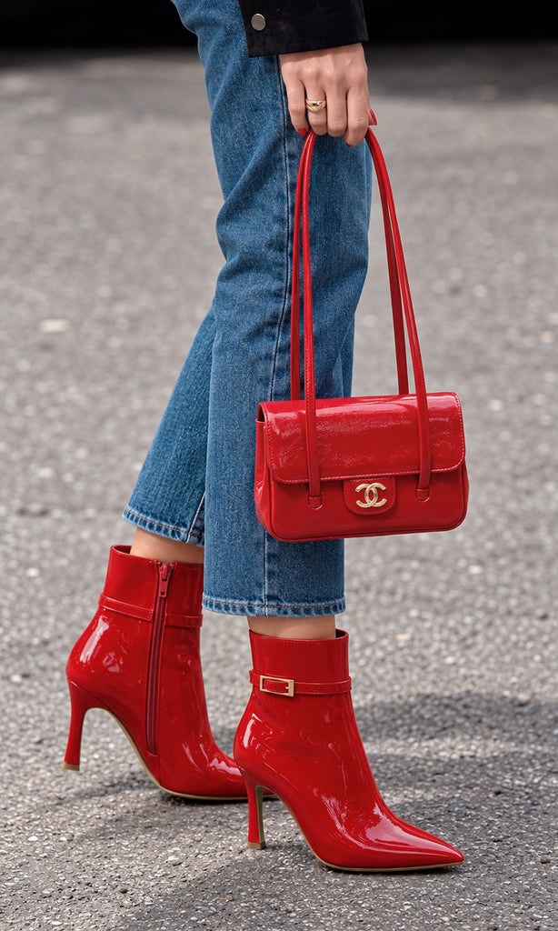 Botines rojos de charol con tacón fino, punta afilada y correa con hebilla, combinados con jeans azules y bolso rojo en un look casual chic
