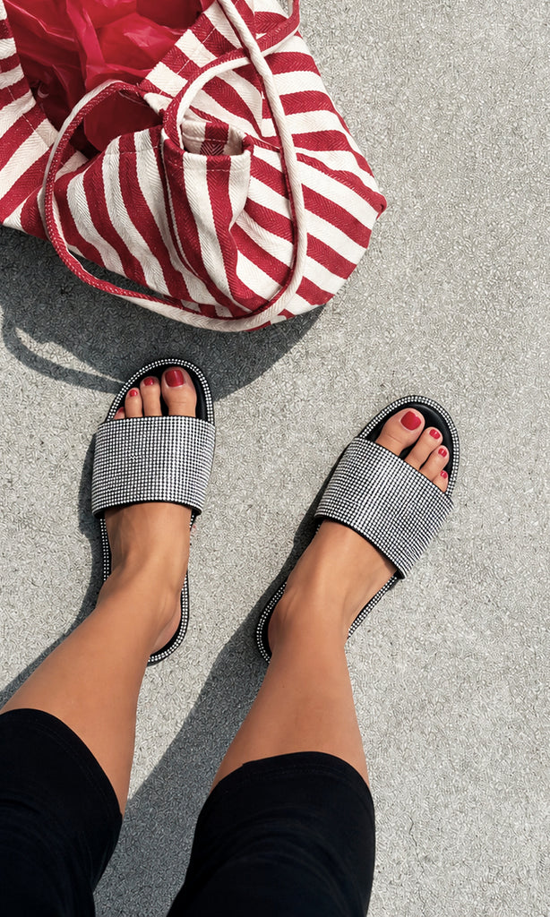 Sandalias de brillos INGRID negras con pedrería plateada, combinadas con un look casual en negro y bolso de rayas para un outfit de verano cómodo y moderno