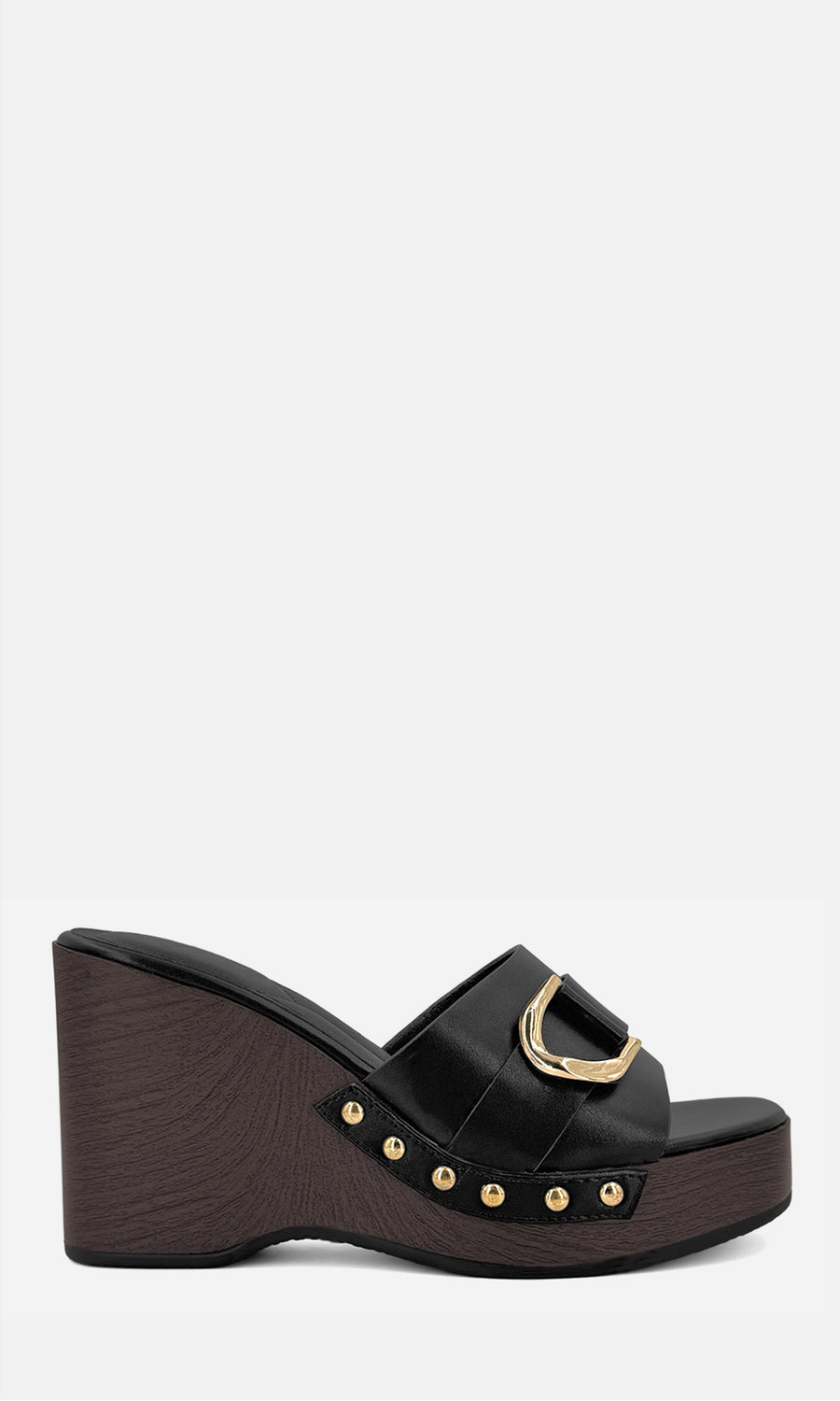 Sandalias negras de plataforma con tacón de cuña, hebilla dorada y detalles de estoperoles, combinadas con pantalón beige de pierna ancha, top negro y bolso cafe