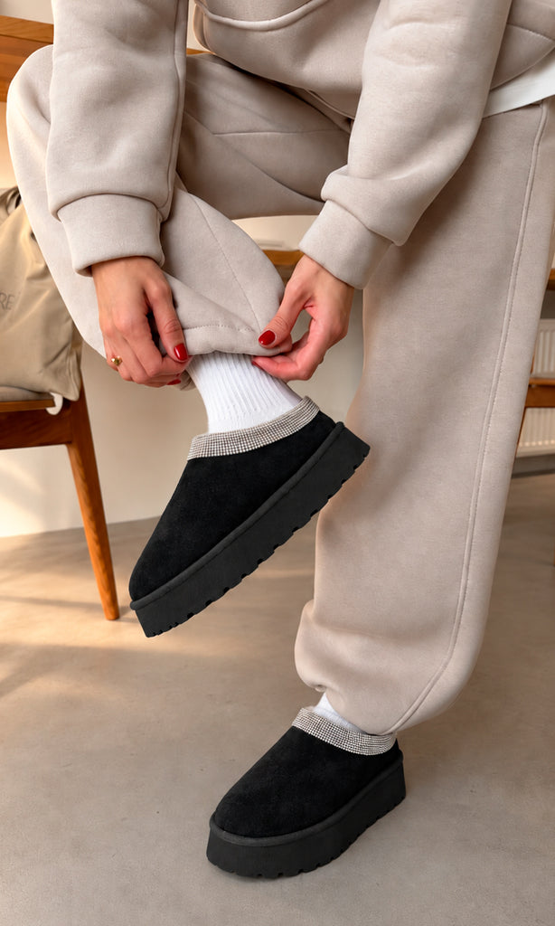 Zuecos Lunna negros con plataforma chunky, acabado tipo gamuza y detalle de cristales alrededor del empeine, estilizados con calcetas blancas y conjunto deportivo beige