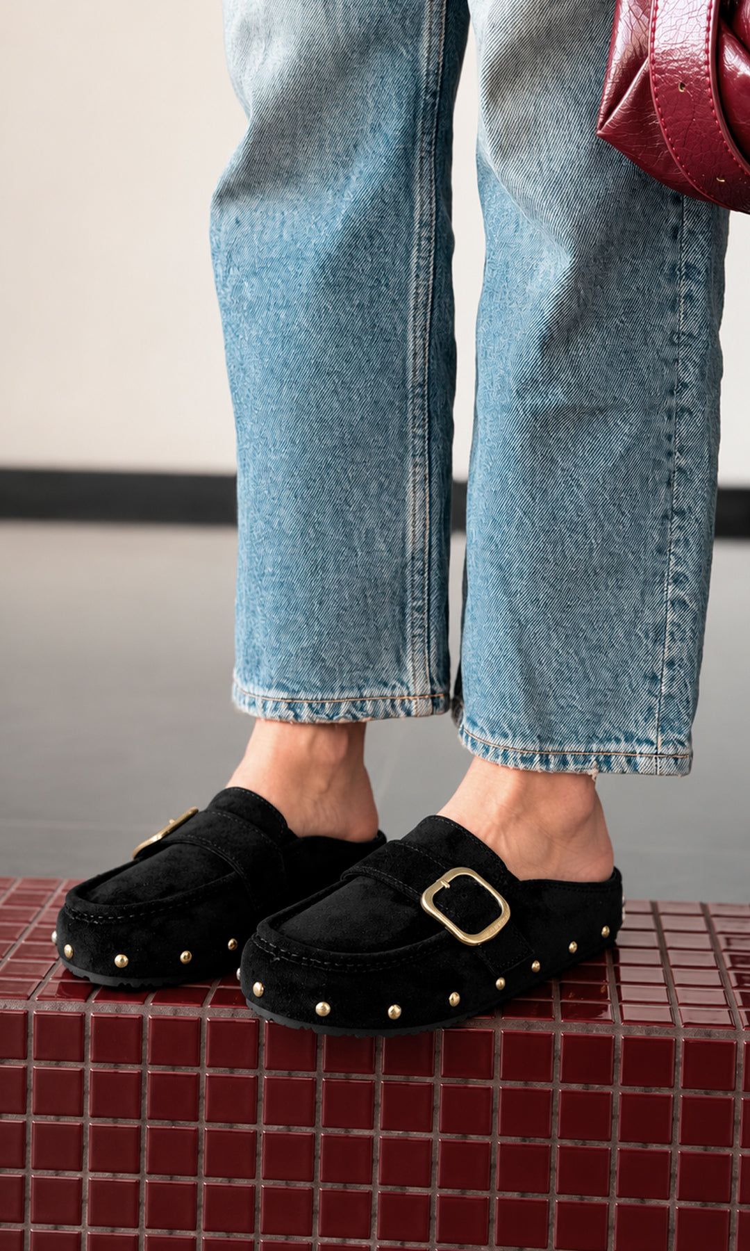 Mules negros con hebilla dorada y estoperoles, combinados con jeans rectos para un look casual