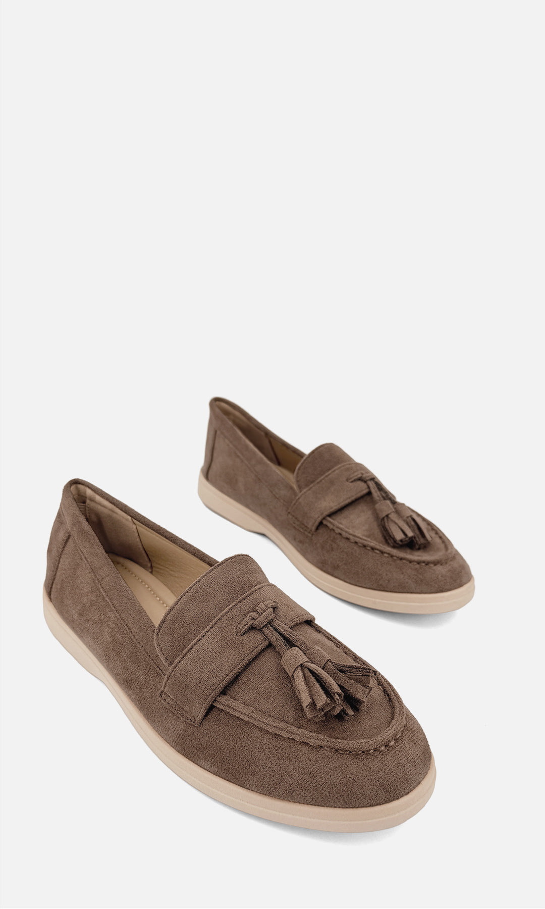Par de mocasines SINATRA TAUPE de gamuza en vista tres cuartos, con borlas frontales, empeine clásico y suela baja en tono beige