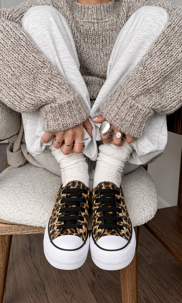 Tenis con estampado de leopardo, agujetas negras y plataforma blanca, combinados con pantalón gris, calcetines blancos y suéter tejido en un look casual relajado