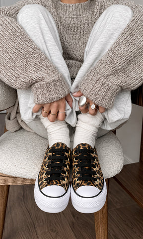 Tenis con estampado de leopardo, agujetas negras y plataforma blanca, combinados con pantalón gris, calcetines blancos y suéter tejido en un look casual relajado