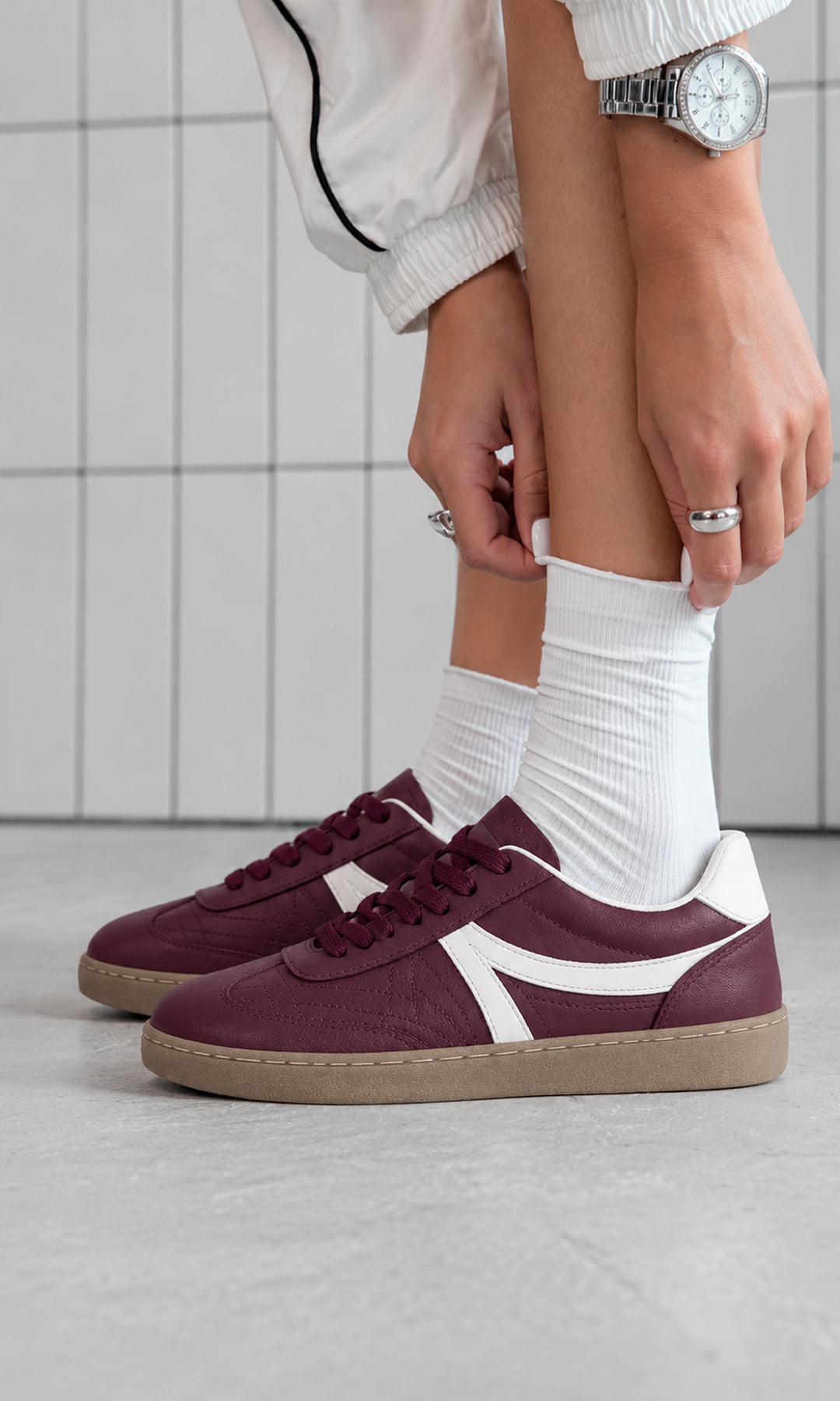 Tenis color vino estilo retro con detalles blancos y suela color caramelo, combinados con calcetas blancas y chaqueta deportiva clara para un look casual urbano