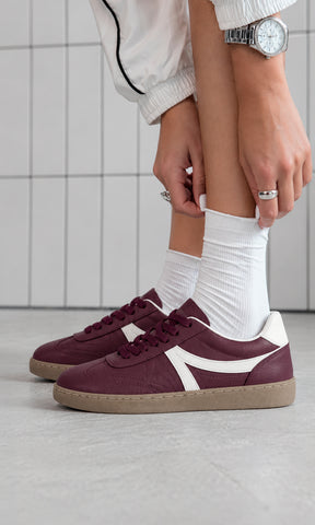 Tenis color vino estilo retro con detalles blancos y suela color caramelo, combinados con calcetas blancas y chaqueta deportiva clara para un look casual urbano