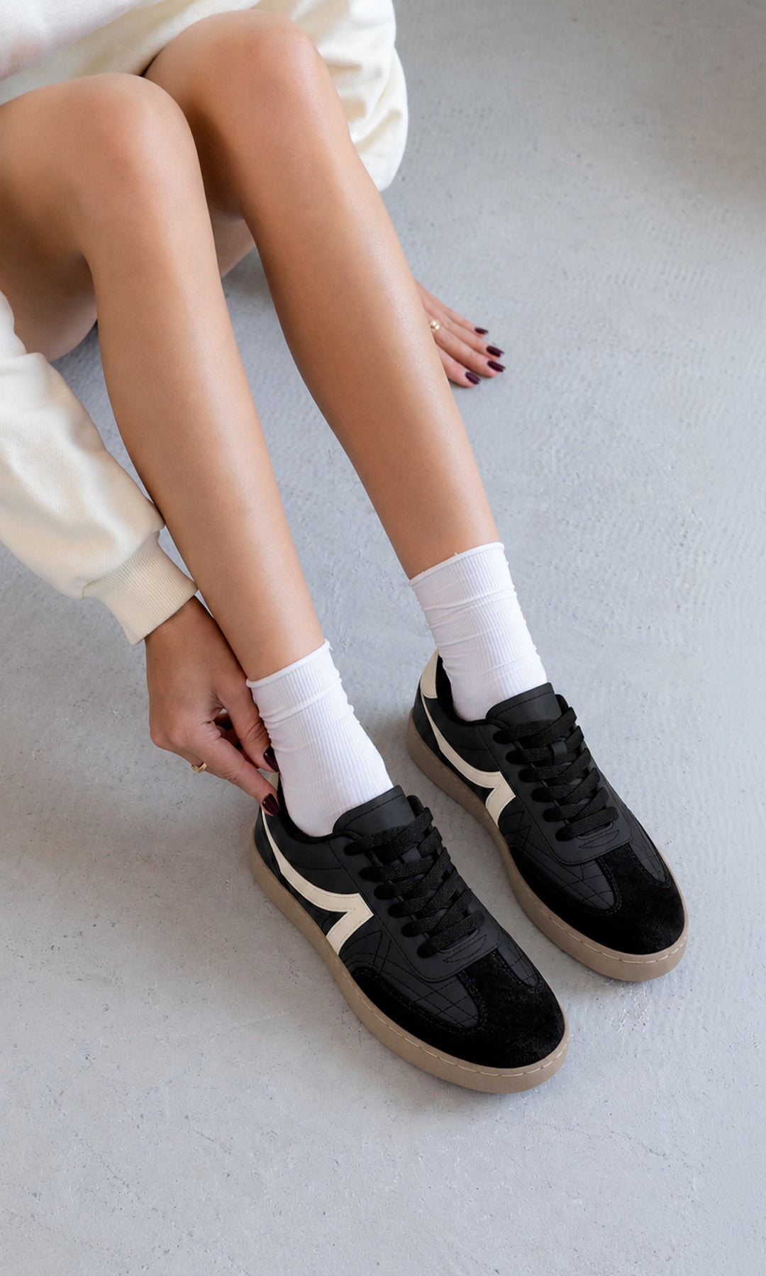 Tenis negros estilo retro con detalles crema y suela color caramelo, combinados con calcetas blancas y sudadera clara en un look casual cómodo para mujer