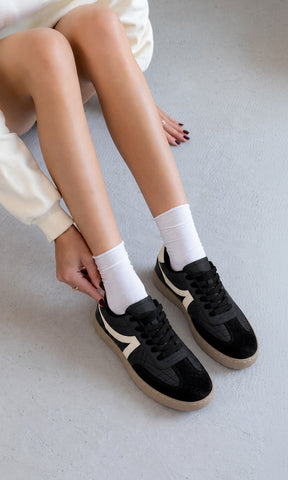 Tenis negros estilo retro con detalles crema y suela color caramelo, combinados con calcetas blancas y sudadera clara en un look casual cómodo para mujer