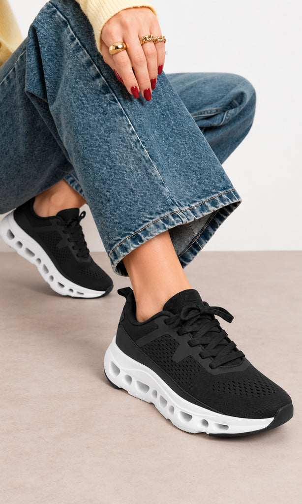 Tenis deportivos negros con tejido transpirable y suela blanca gruesa, combinados con jeans anchos y prendas claras en un look casual y cómodo para mujer