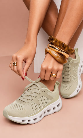 Tenis deportivos nude con tejido transpirable, cordones y suela blanca gruesa con diseño de cámara, presentados en un look casual en tonos neutro