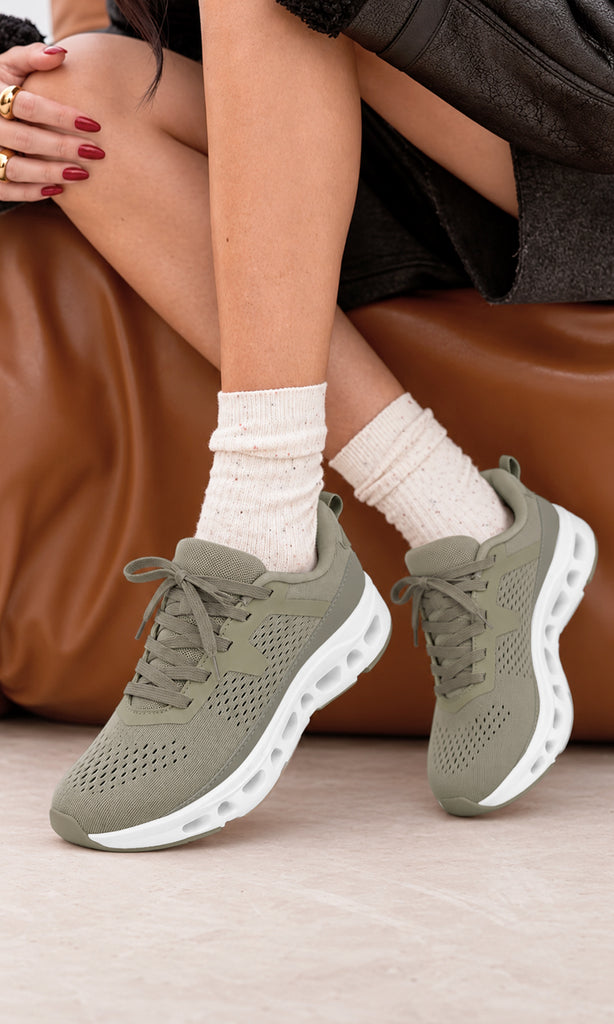 Tenis deportivos taupe con tejido transpirable y suela blanca gruesa, combinados con calcetas de punto y prendas oscuras en un look casual de diario